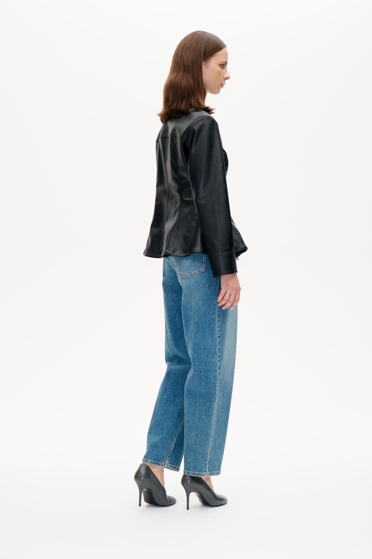 Mannequin de profil portant une veste noire brillante au col marron texturé, un jean bleu et des escarpins noirs.