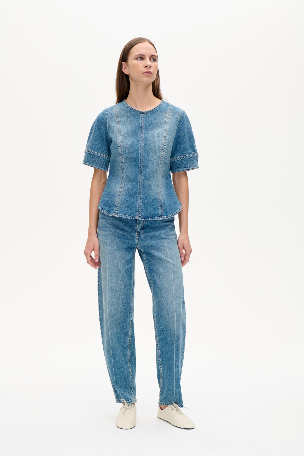 Vue de face d'un mannequin portant un top en denim bleu à manches courtes, encolure ronde et empiècements verticaux marqués, associé à un jean.