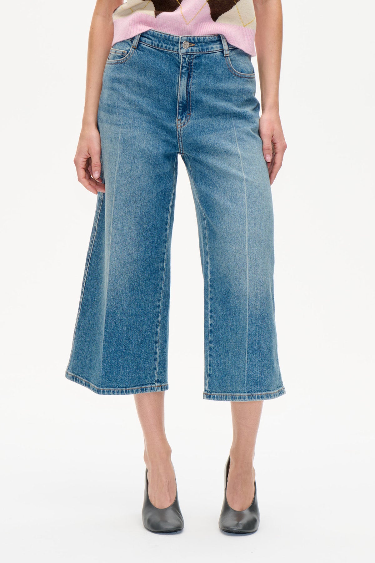 Front view of wide-leg, cropped blue jeans with a faded wash, worn with a pink-and-cream patterned knit top.