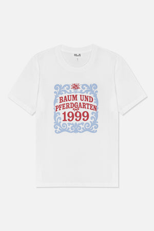 Front view of a white short-sleeved T-shirt with a blue ornamental frame, red floral detail and “Baum und Pferdgarten 1999” text.