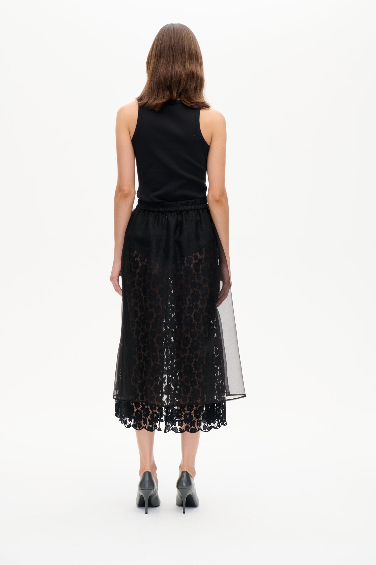 Back view of a model wearing a black ribbed sleeveless top and sheer black lace skirt with a scalloped hem.