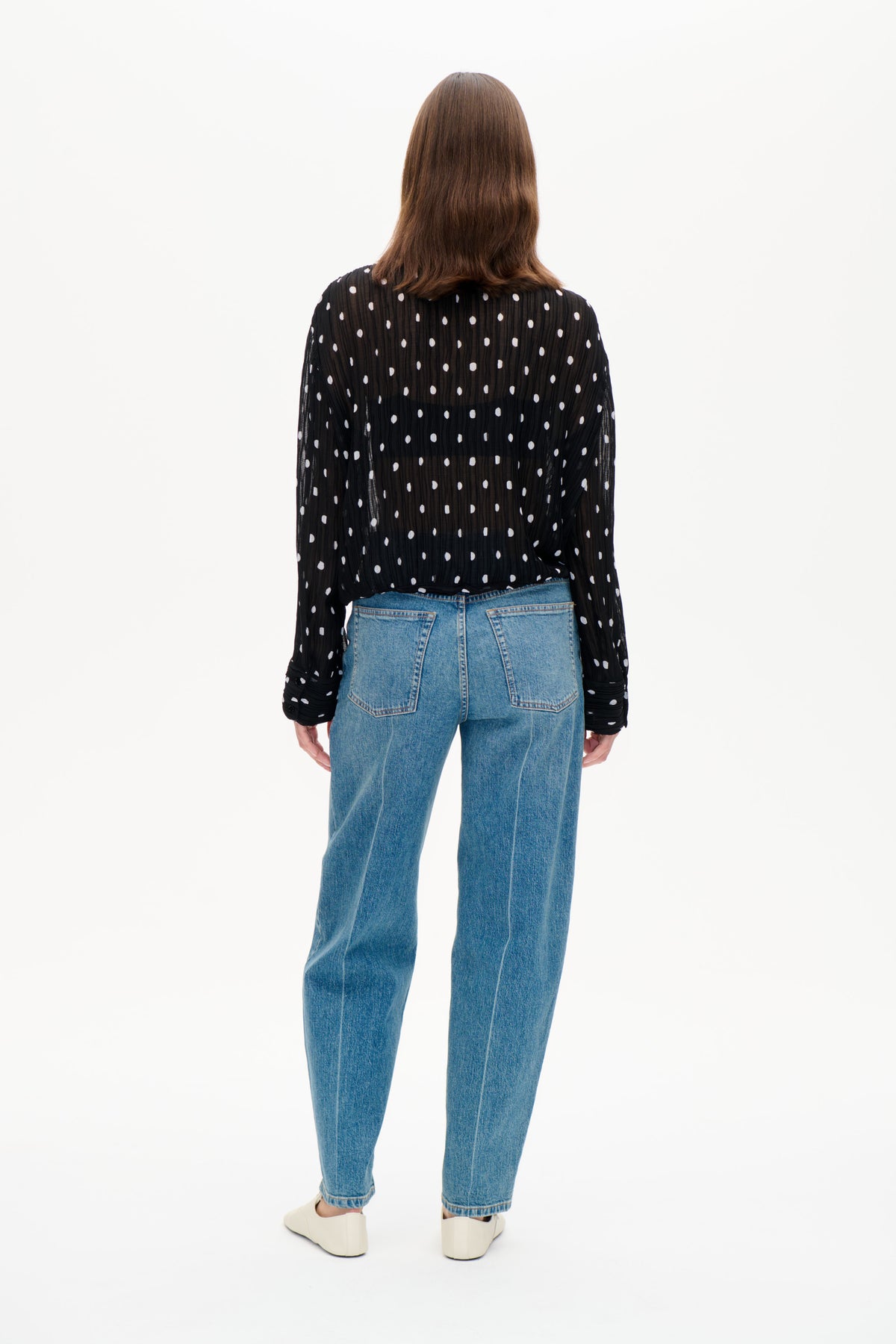 Rückenansicht einer schwarzen transparenten Langarmbluse mit weißen Punkten, kombiniert mit blauen Jeans.