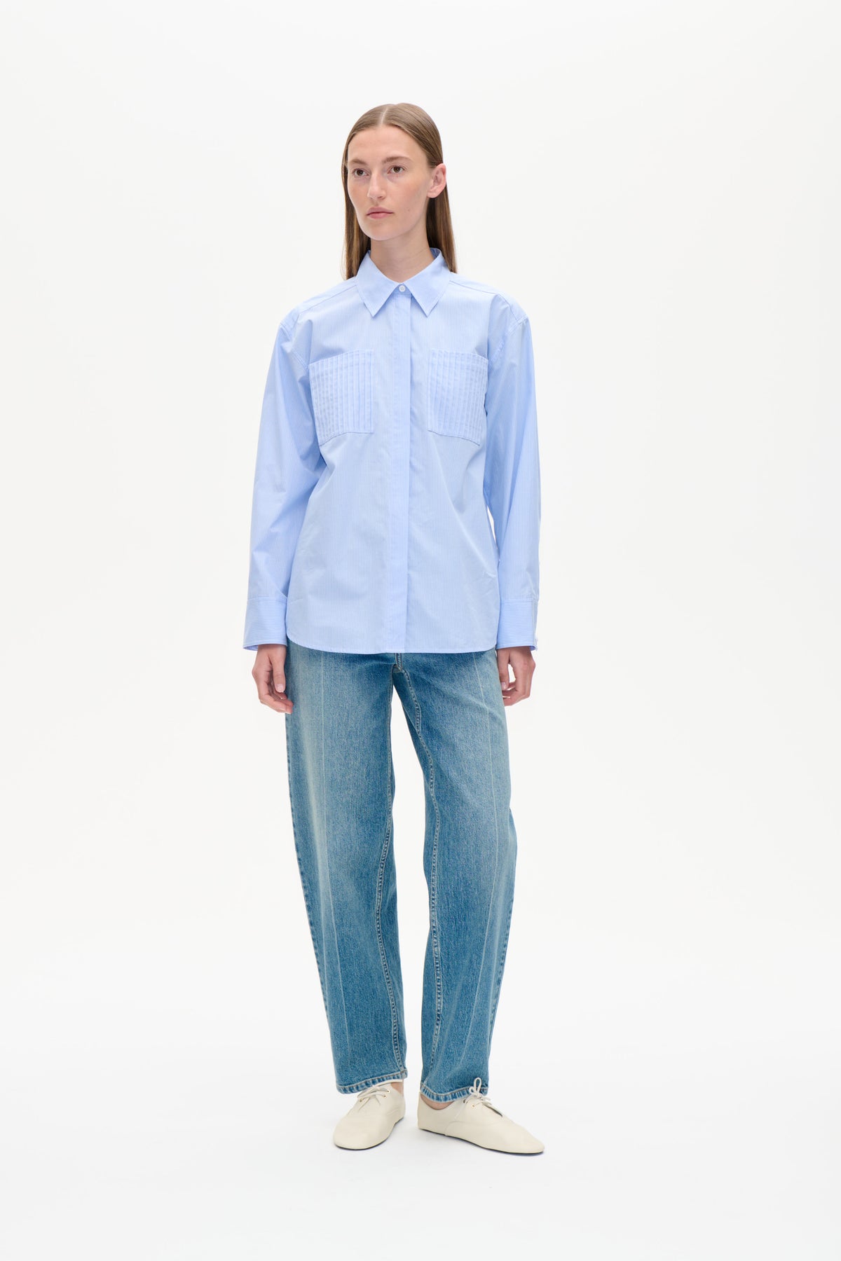 Model wearing a light blue finely striped button-front shirt with a pointed collar and two large chest pockets, shown from the front.
