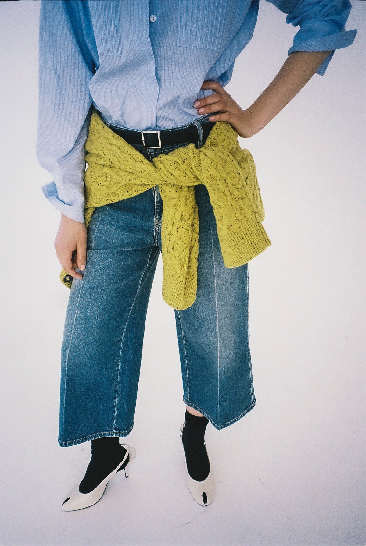 Ausschnitt einer Kampagnenaufnahme: hellblaue Bluse mit Knopfleiste, weite blaue Jeans und senfgelber Pullover, in der Taille gebunden.
