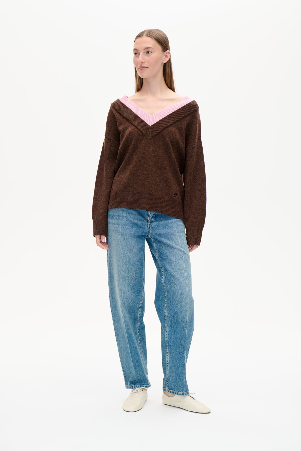 Front view of a brown knit sweater with a wide pink V-neck trim, styled with light blue jeans.