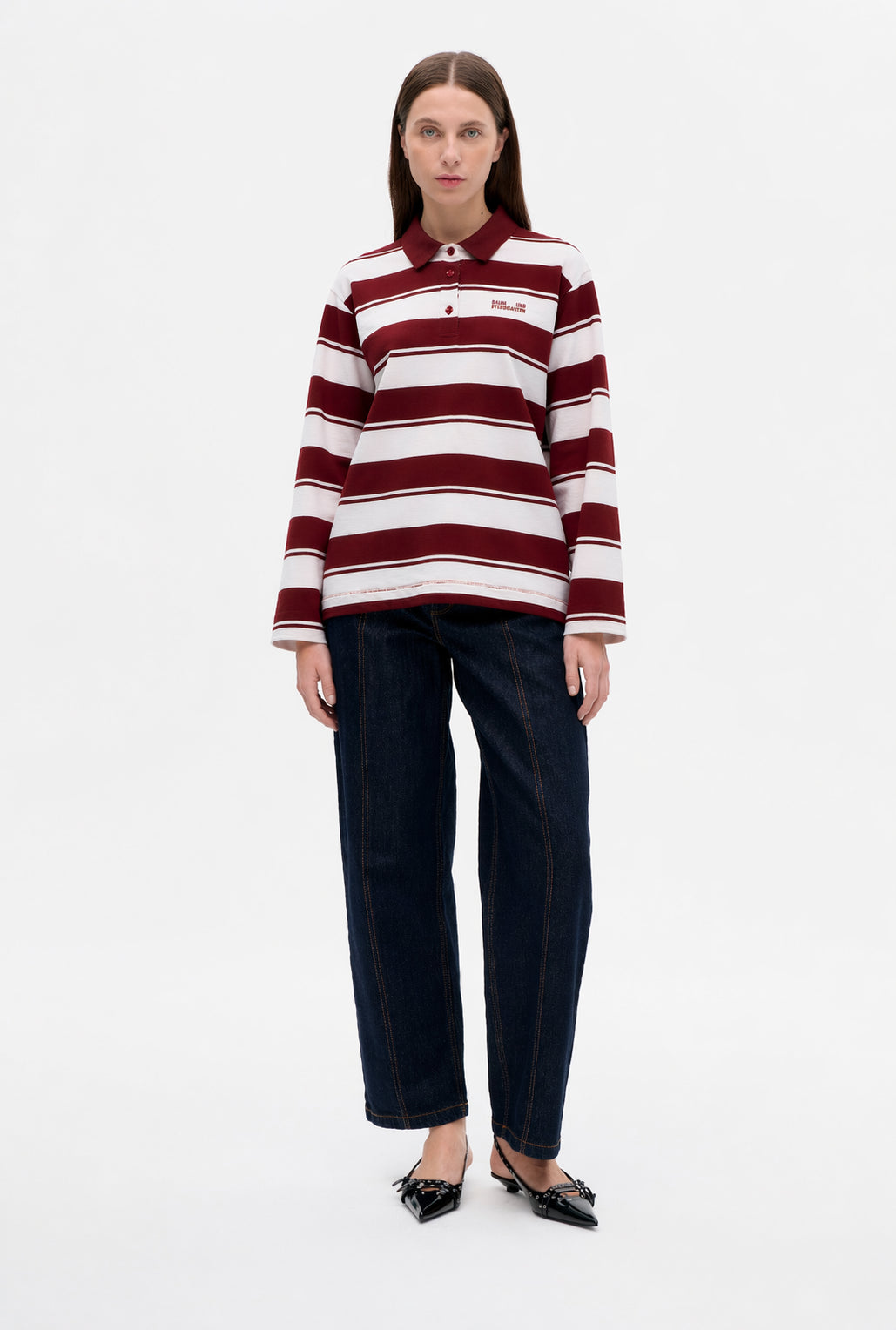 Front view of a model wearing a burgundy-and-white striped long-sleeve polo shirt with a small chest logo and dark wide-leg jeans.