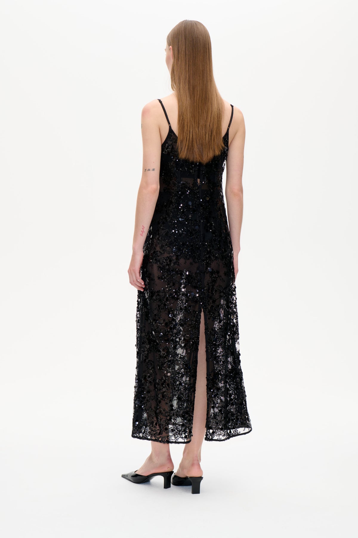 Back view of a black sheer midi dress with thin straps and all-over sequins, modeled against a plain white background.