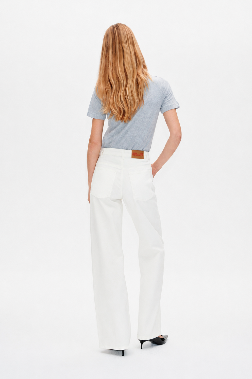Back view of a model wearing a pale blue short-sleeved T-shirt and white wide-leg jeans with back pockets.