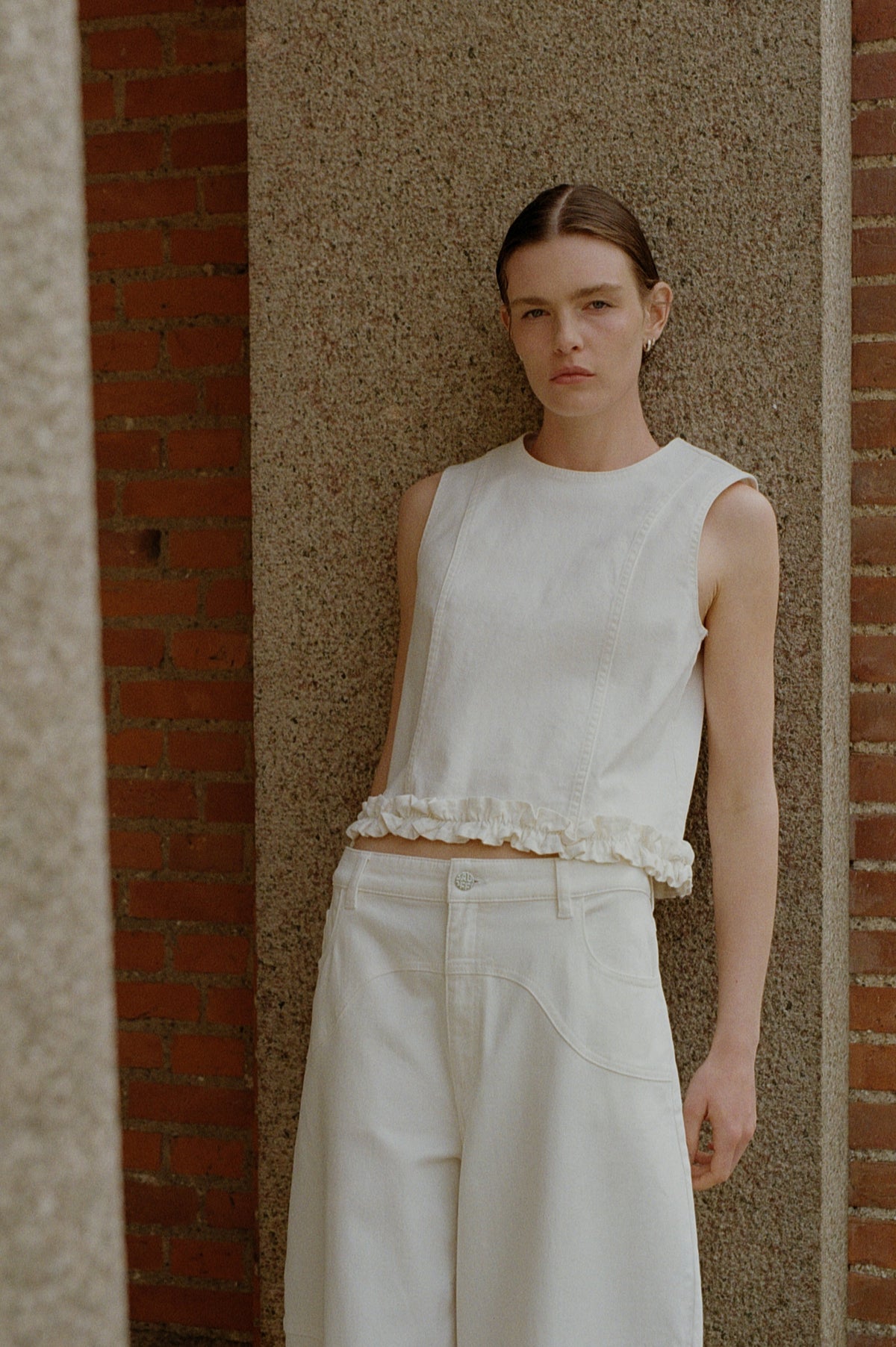 Front campaign portrait of a model in a white sleeveless top with a ruffled hem and a white skirt with curved seam details