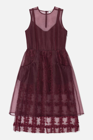 Front view of a burgundy sleeveless dress with a sheer overlay, round neckline, side pockets and floral lace detailing.
