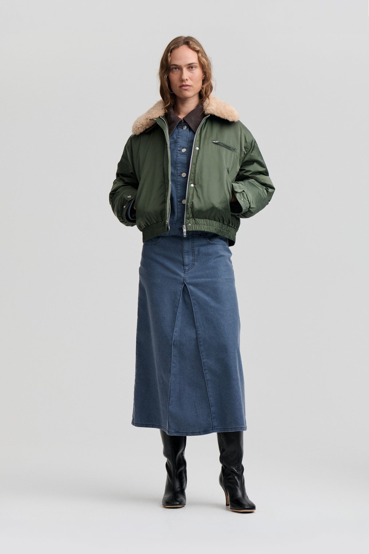 Front view of a model wearing a dark green jacket with a cream pile collar over a blue denim midi dress.