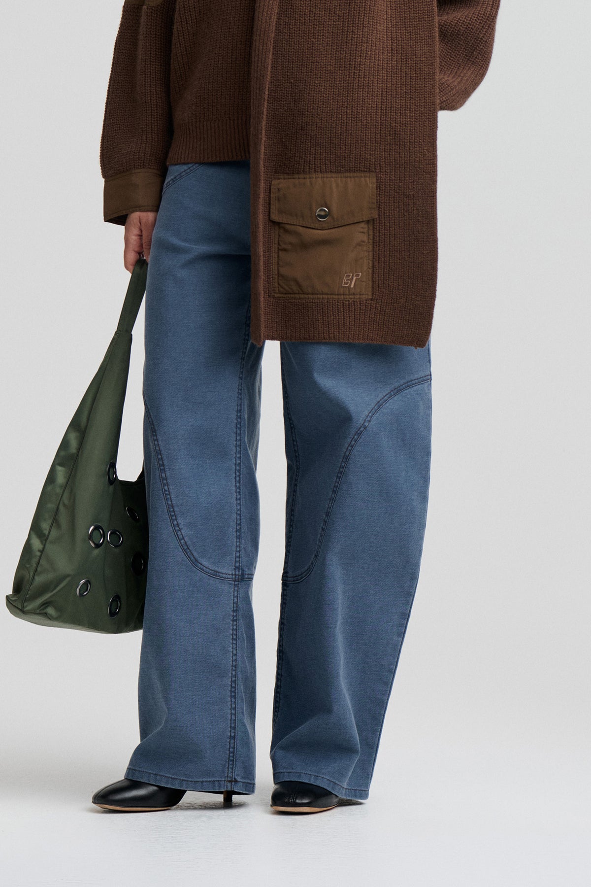 Close-up of a brown textured knit cardigan with a flap pocket and button, worn over blue jeans.